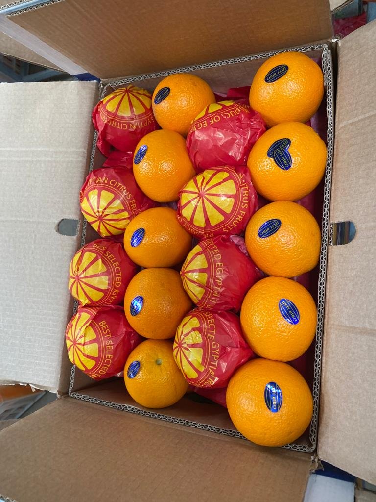 A box of oranges, some wrapped in branded red and yellow paper.