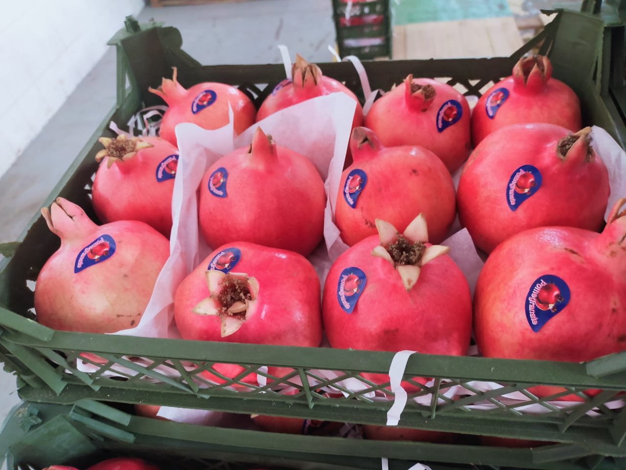 Pomegranates with stickers packed in a green plastic crate.